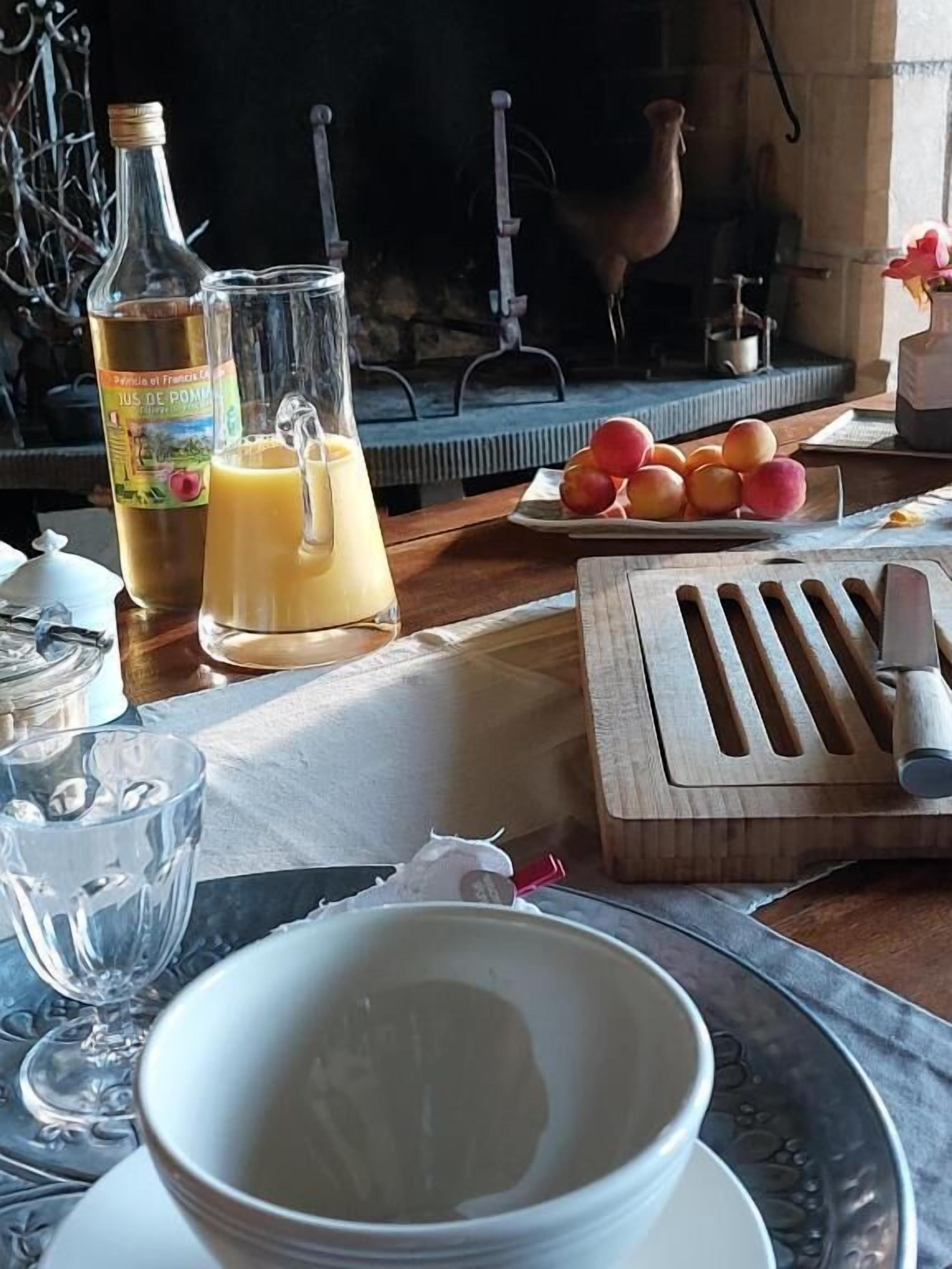 Una mesa de desayuno con una botella de jugo, un vaso, un plato de fruta y una tabla de madera.
