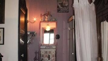 A narrow hallway leading to a bathroom with a sink, mirror, and shower area.
