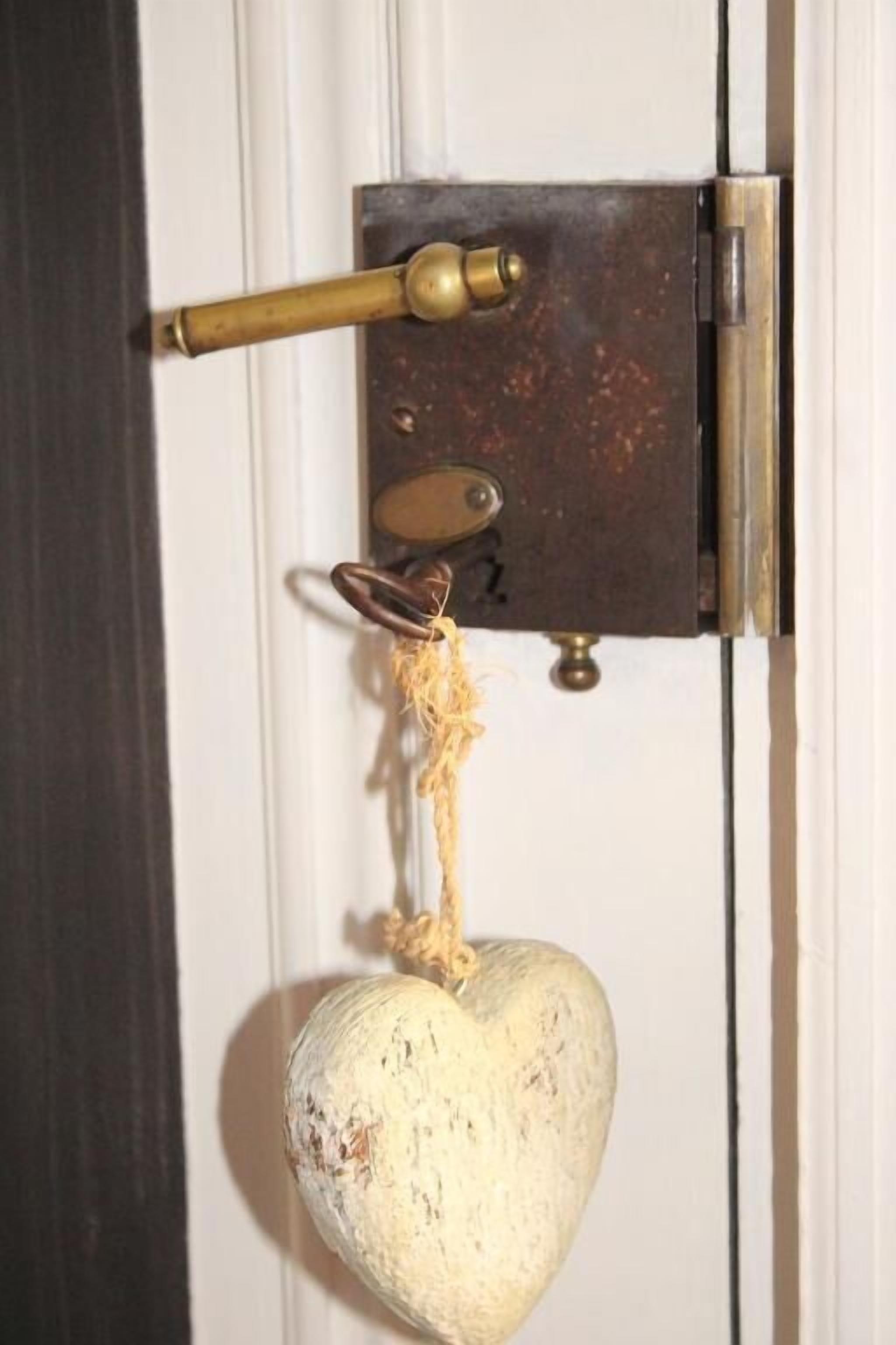 Een deur met een koperen knop, een metalen grendel en een hartvormige decoratie die aan de knop hangt.