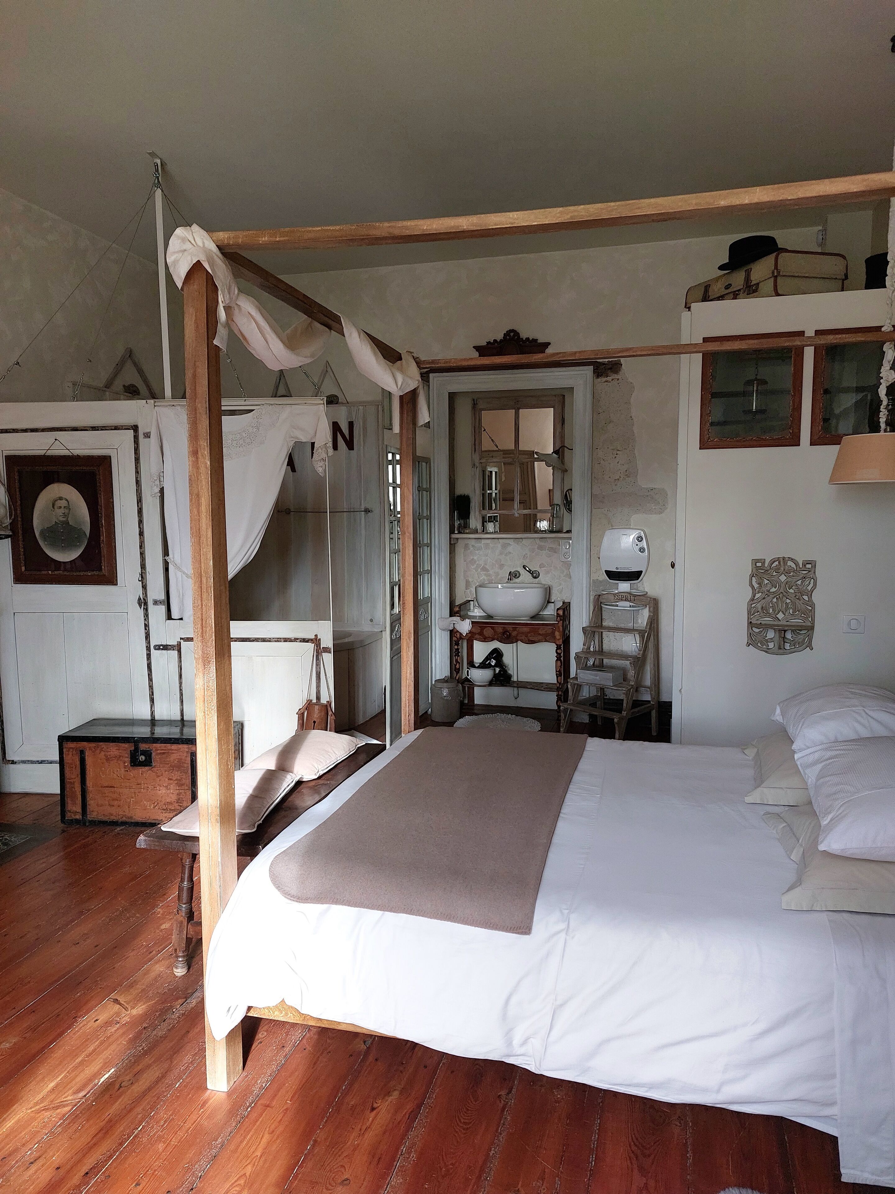 Quarto com cama de dossel, cômoda de madeira, espelho e pequena mesa com abajur.