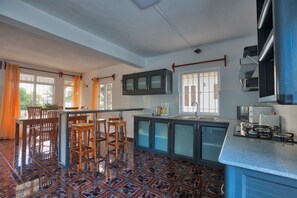 Une cuisine avec un coin bar, des chaises en bois, un sol carrelé et une fenêtre avec des rideaux.