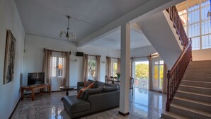 A spacious living area with a large sofa, a television, and a staircase leading to an outdoor area.