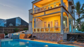 A two-story house with a swimming pool, a balcony, and a stone wall.