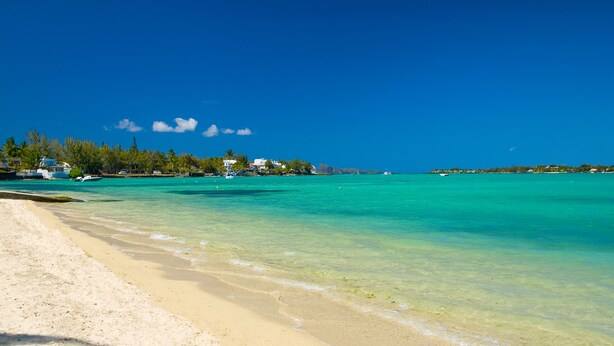 A beach with clear turquoise water, a sandy shore, and buildings in the background.