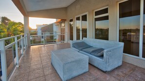 A covered patio area with a wicker sofa and ottoman, large windows, and a view of the surrounding landscape.