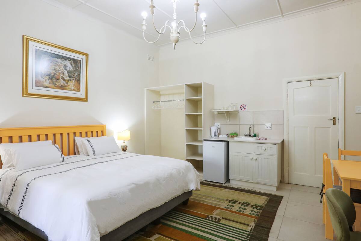 Ein Schlafzimmer mit Bett, Nachttisch, Lampe, Kleiderschrank und einer kleinen Küchenzeile.