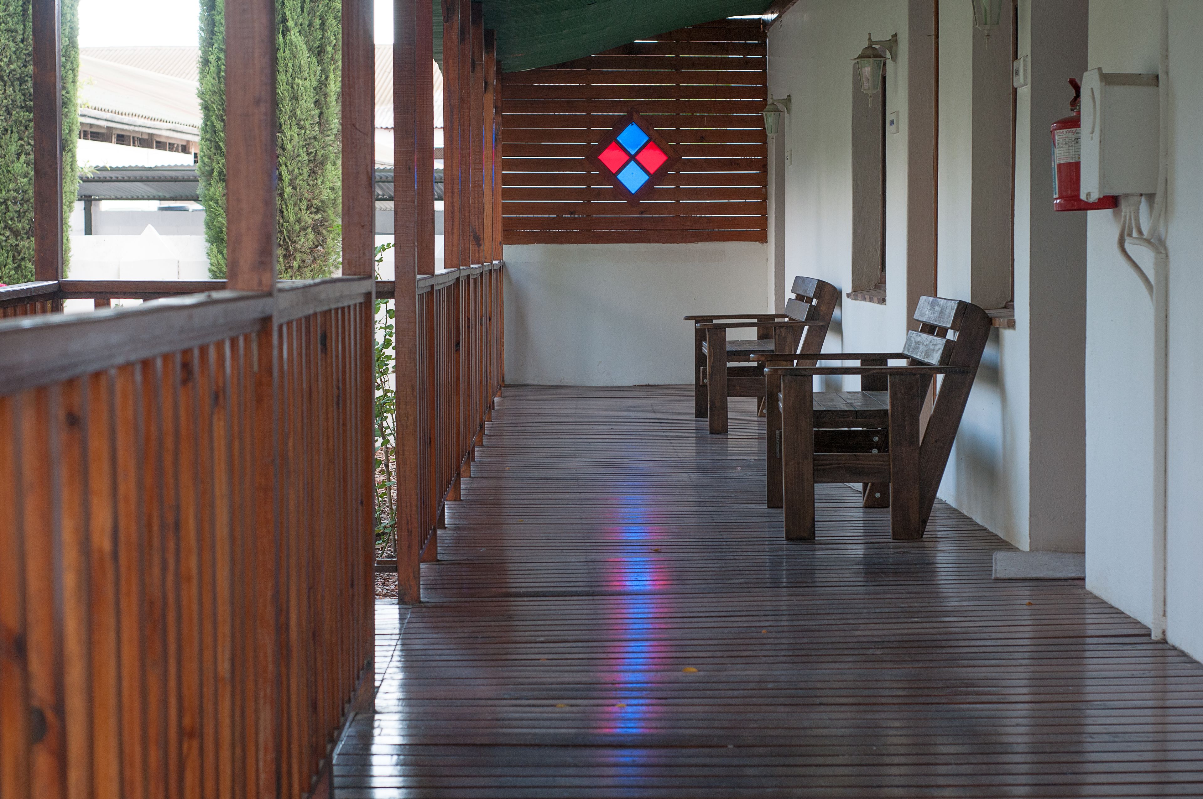 A wooden deck with a table and chairs, a wall-mounted fire extinguisher, and a decorative wall piece.