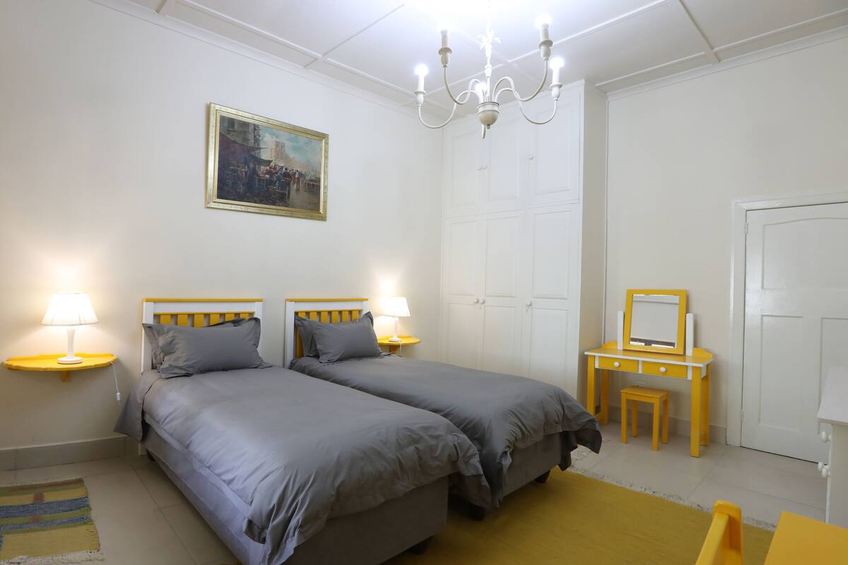 Ein Schlafzimmer mit zwei Betten, Nachttischlampen, einem Schminktisch, einem Spiegel und einem Bild an der Wand.