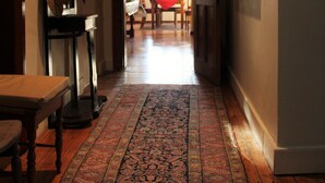 A hallway with a patterned rug, a dining area with a red tablecloth, and hats hanging on the wall. - Green Olive Guesthouse (Robertson)