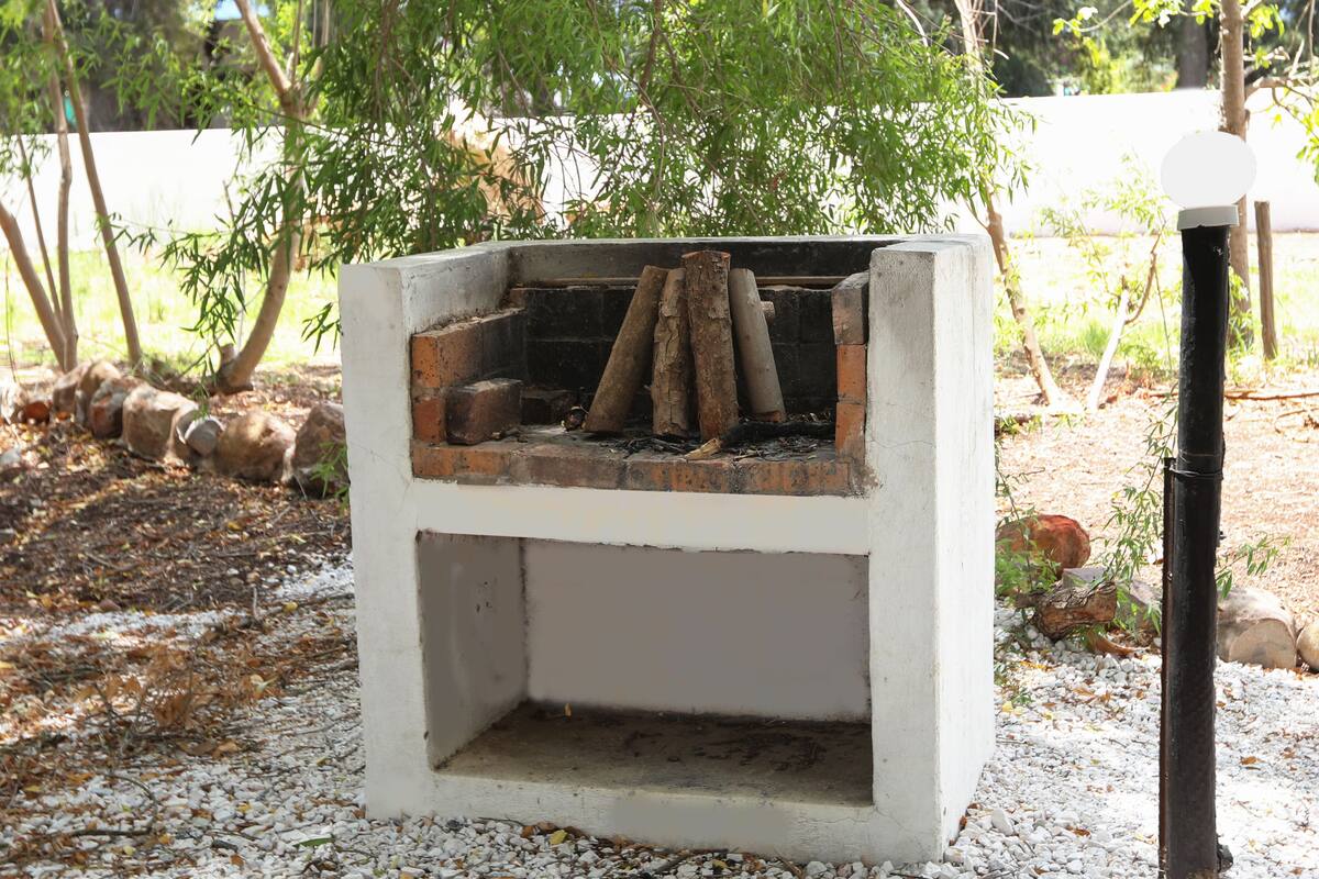 Ein Beton-Grill im Freien mit Feuer, umgeben von Kies und Bäumen.