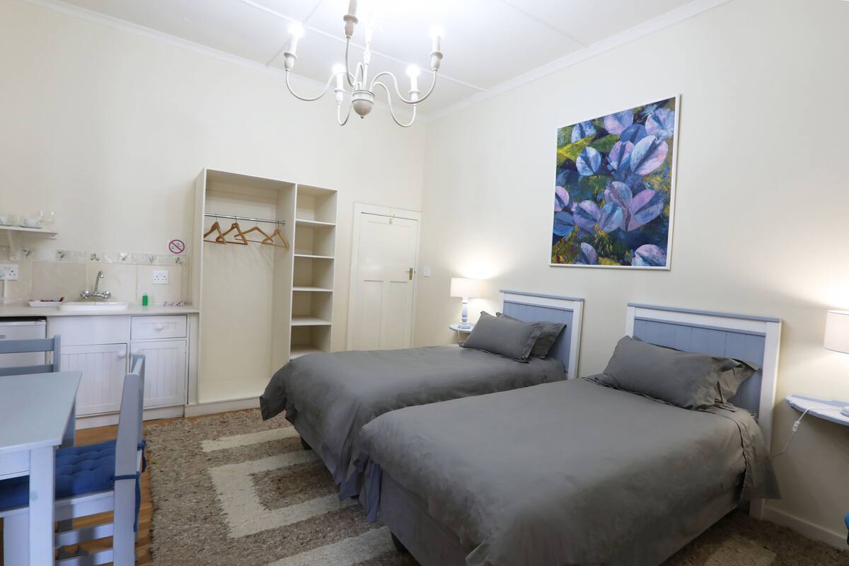 Ein Schlafzimmer mit zwei Betten, einem Schreibtisch, einem Stuhl, einem Kleiderschrank und einem Bild an der Wand.