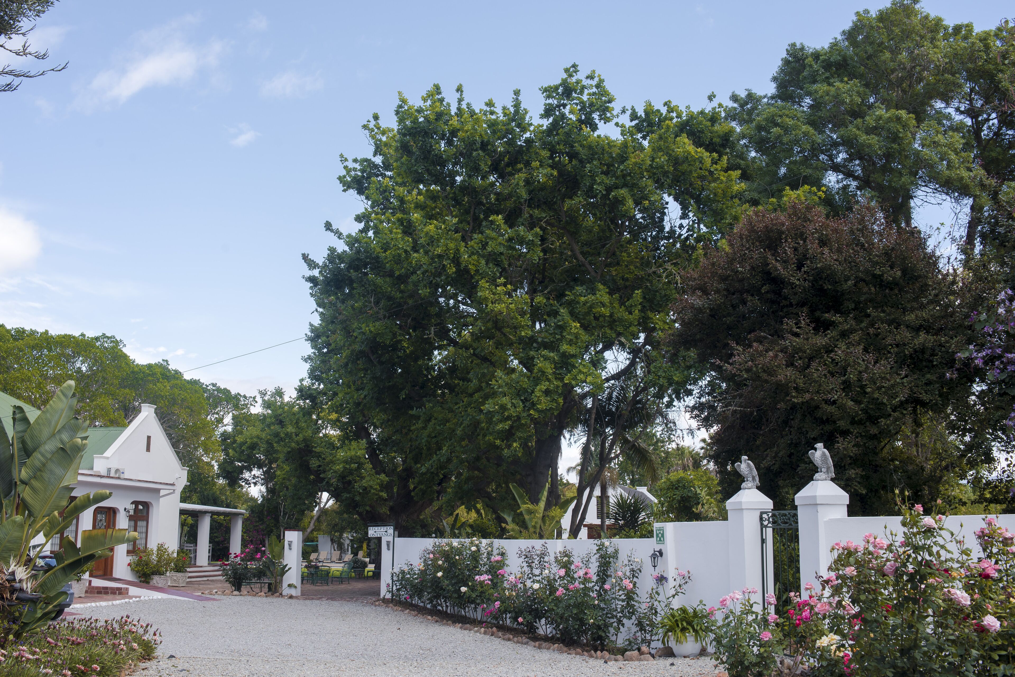 A white building with a green roof, surrounded by a white fence and flowering plants.