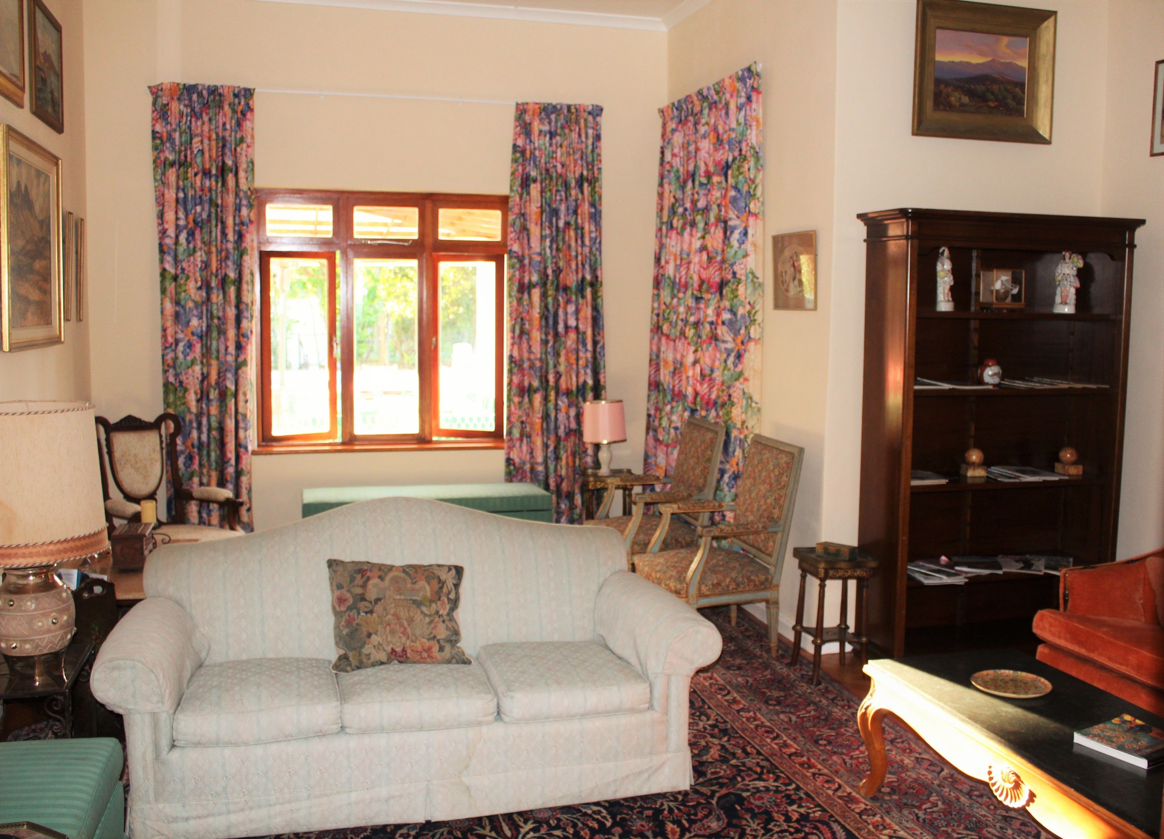 Quarto com sofá, cadeiras, estante de livros e janela com cortinas.