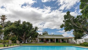 A swimming pool with a house in the background, surrounded by trees and a clear sky. - Green Olive Guesthouse (Robertson)