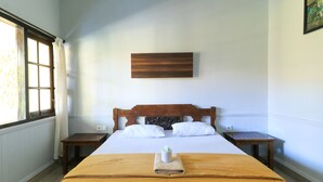 A neatly made bed with a brown bedspread, white pillows, and a small white vase on the center. There is a wooden headboard, two bedside tables, and a wall-mounted artwork above the bed. - Sari Indah Cottages (Kuta)