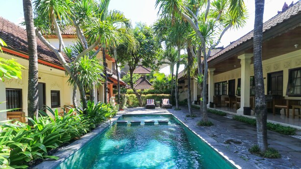 A swimming pool surrounded by palm trees and traditional architecture. - Sari Indah Cottages (Kuta)