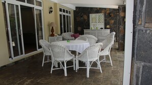 Uma área de refeições com cadeiras de vime branco e uma mesa redonda, paredes de pedra e vista para o exterior.