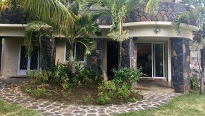 Uma casa com fachada de pedra, um caminho de pedra e palmeiras.