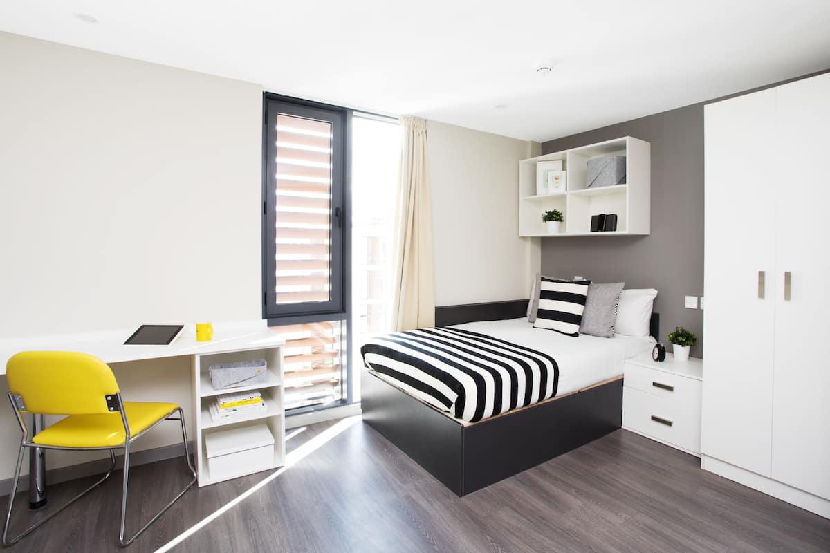 A modern bedroom with a bed, a desk, a chair, and a wardrobe.