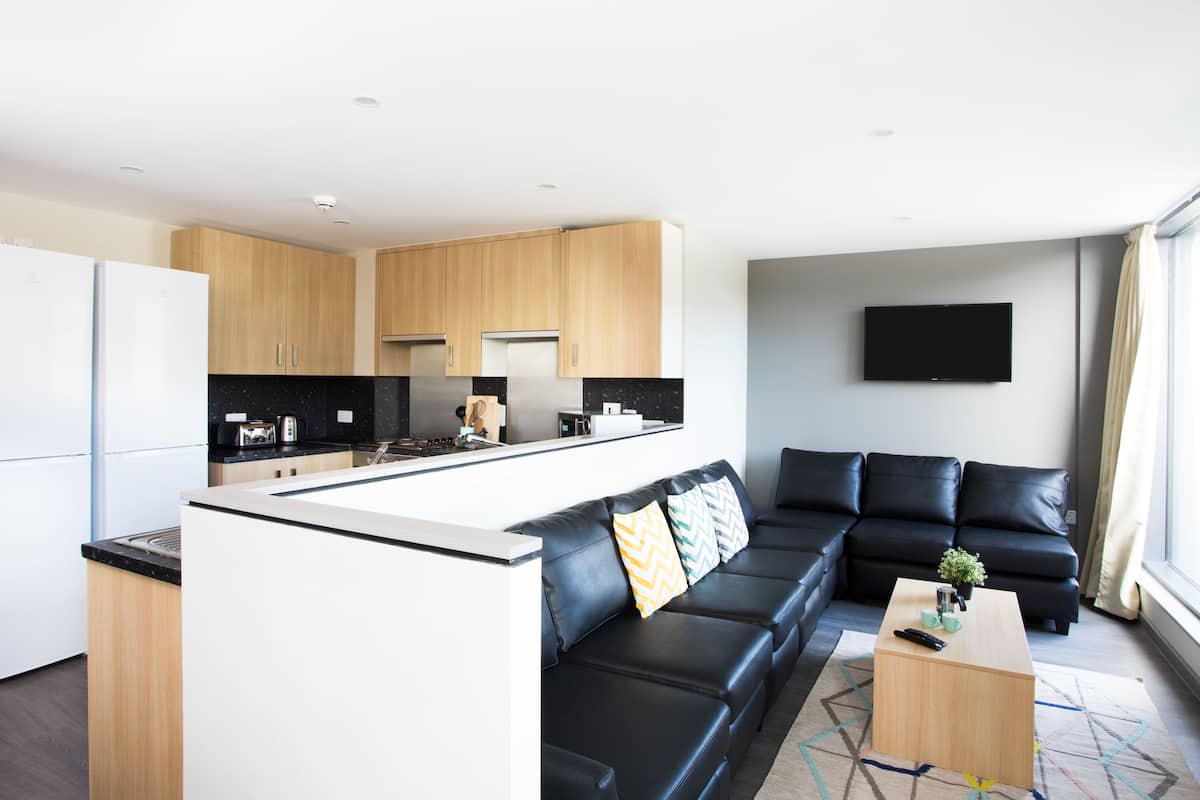 A modern kitchen with a central island, a black leather sofa, and a flat-screen TV mounted on the wall.