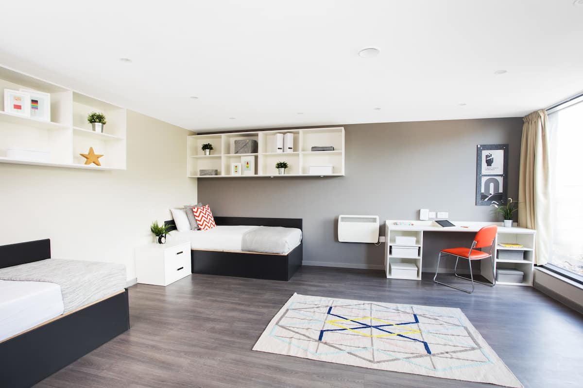 A modern bedroom with a bed, desk, and chair, a built-in wardrobe, and a large window.