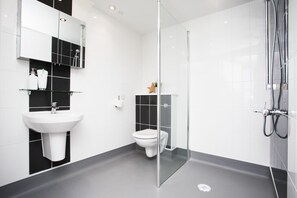 Un baño moderno con cabina de ducha de vidrio, un lavamanos blanco y un inodoro.