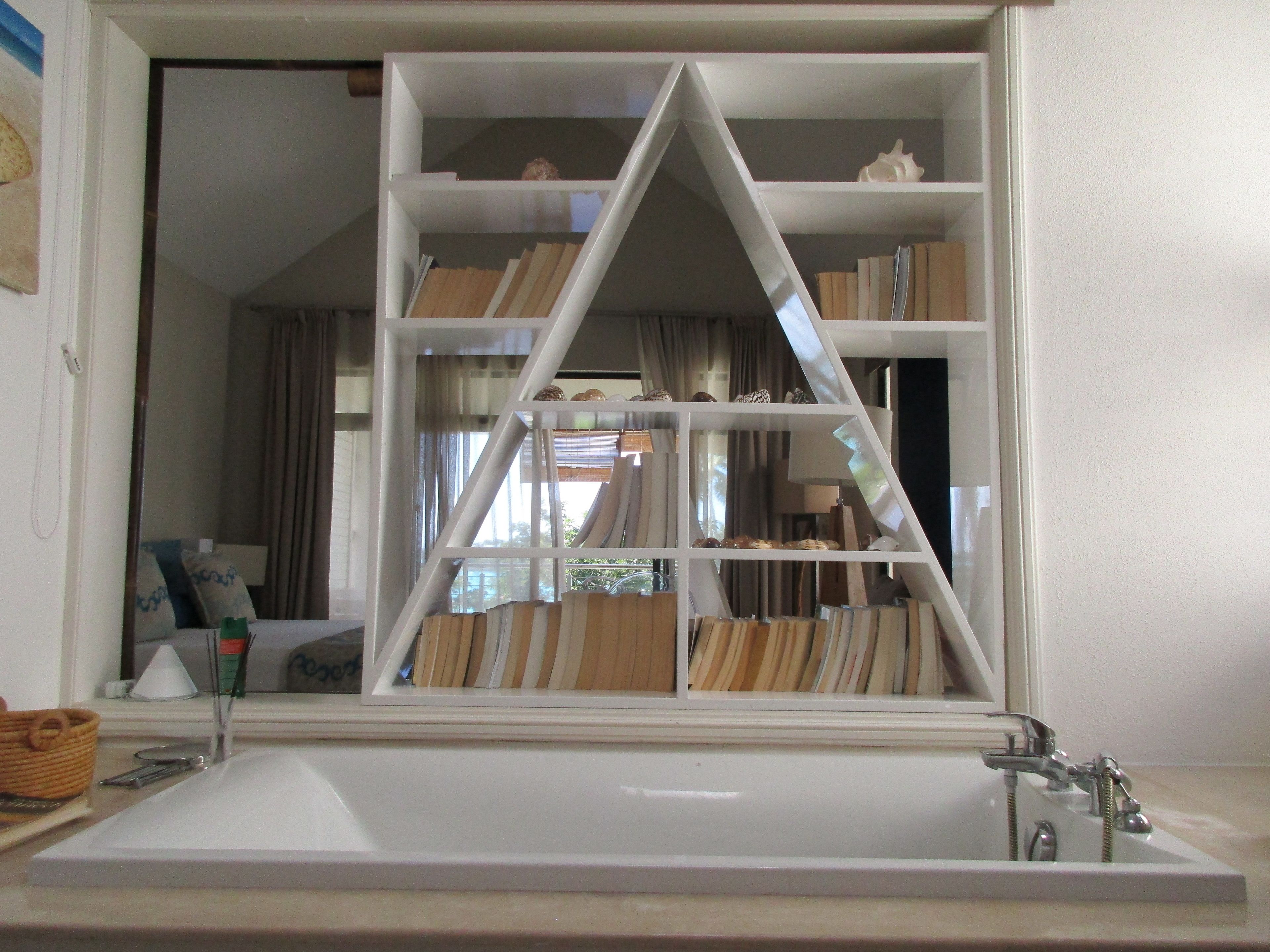 A bathroom with a large white bathtub, a mirror, and a triangular shelving unit above the sink.