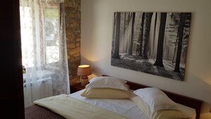 A neatly made bed with white linens and pillows, a wall-mounted painting of a forest, and a lamp on a bedside table. - Agroturizam Stelio (Marcana)