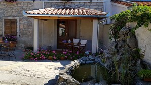 A stone building with a tiled roof, outdoor seating, and a small water feature. - Agroturizam Stelio (Marcana)