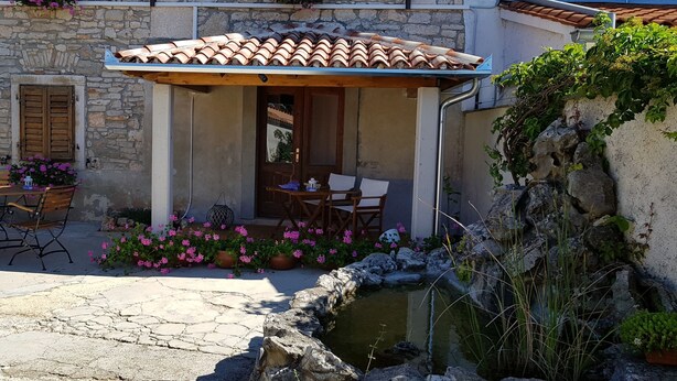A stone building with a tiled roof, outdoor seating, and a small water feature. - Agroturizam Stelio (Marcana)