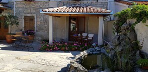 Un edificio de piedra con techo de tejas, mesas al aire libre y una pequeña fuente.