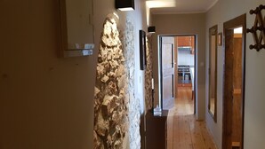 A hallway with a stone accent wall, wooden flooring, and a kitchen visible through an open door. - Agroturizam Stelio (Marcana)