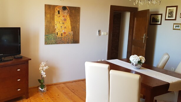 A room with a wooden TV stand, a painting, a dining table with chairs, and a chandelier. - Agroturizam Stelio (Marcana)