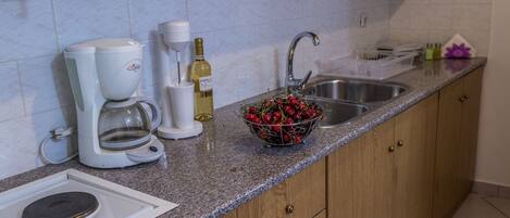 Una cocina con cafetera, botella de vino, un bol de cerezas y un lavabo.