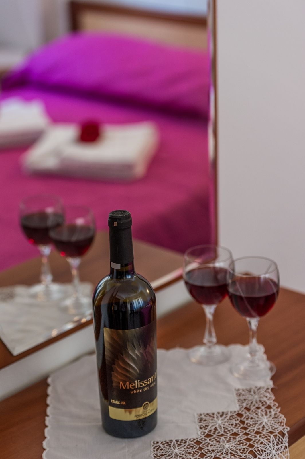 Una botella de vino blanco seco Melissart sobre una mesa con dos copas de vino tinto.