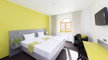 A hotel room with a bed, a desk, a chair, a TV, and a window with a view of the outside.