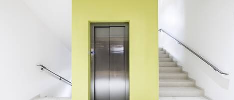 A modern elevator with a metallic finish, flanked by white walls and a yellow accent wall.