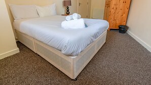 A neatly made bed with white linens, a wooden wardrobe, and a small trash bin. - Perfect Flat in Central Edinburgh (Edinburgh)
