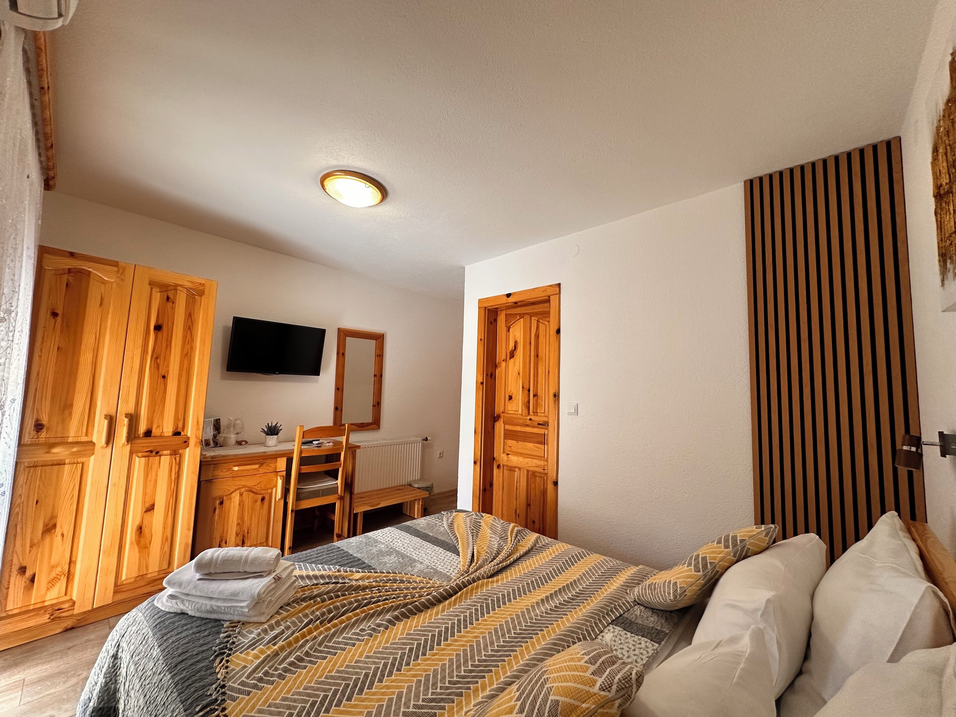 A bedroom with wooden furniture, a bed with patterned bedding, a television, and a mirror on the wall.