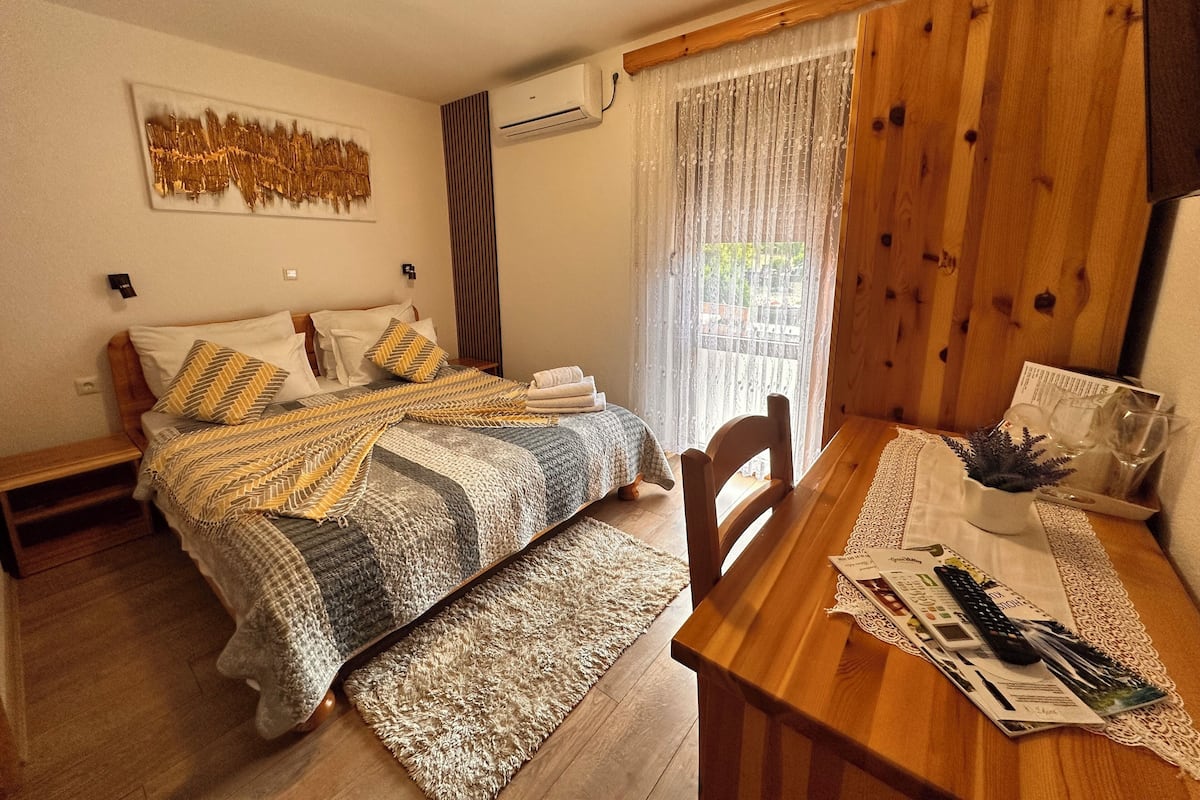 Un dormitorio con una cama de madera, una mesa de comedor de madera y un ventanal con cortinas.