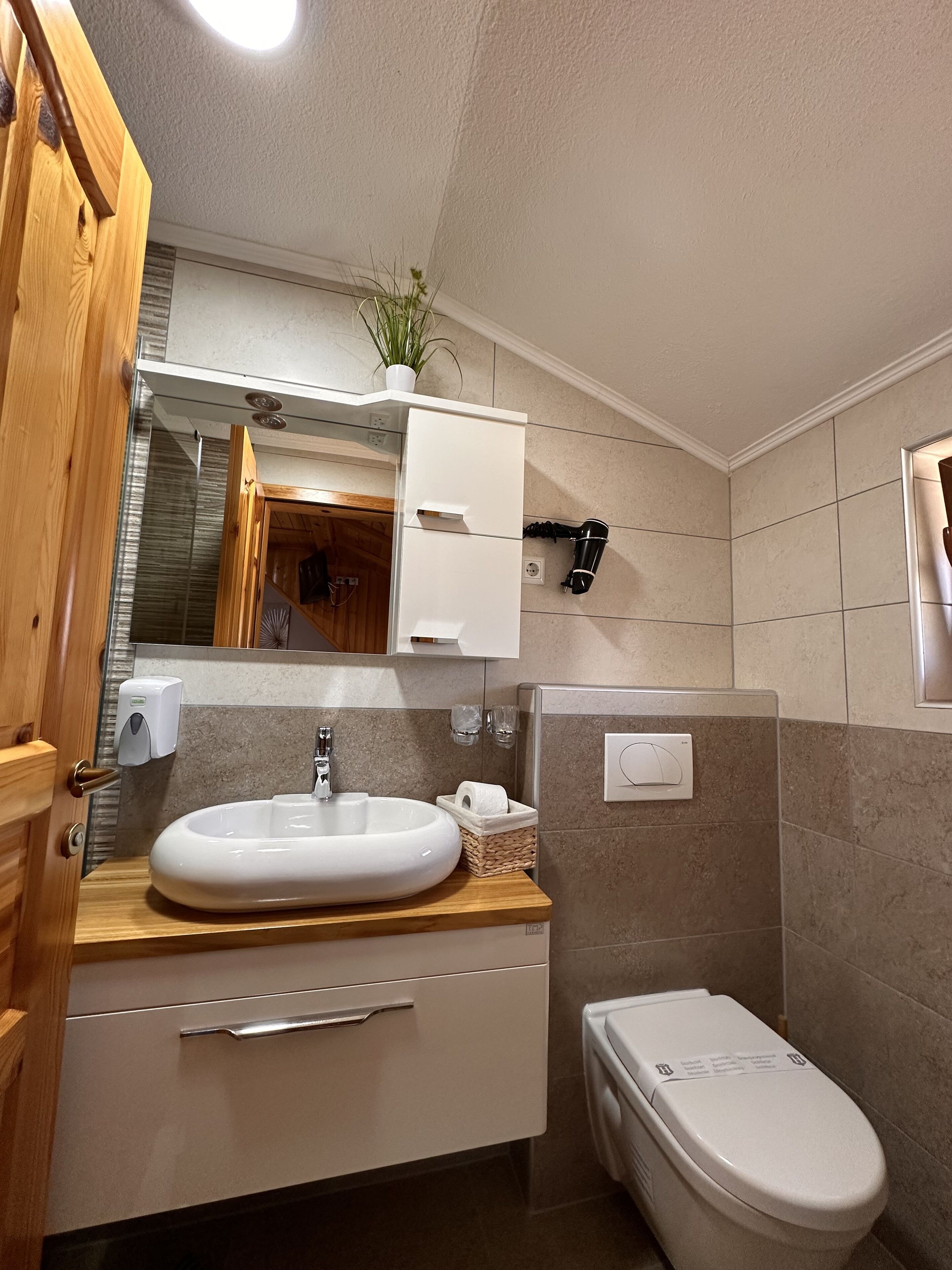 Un baño moderno con tocador de madera, lavamanos, inodoro y espejo.