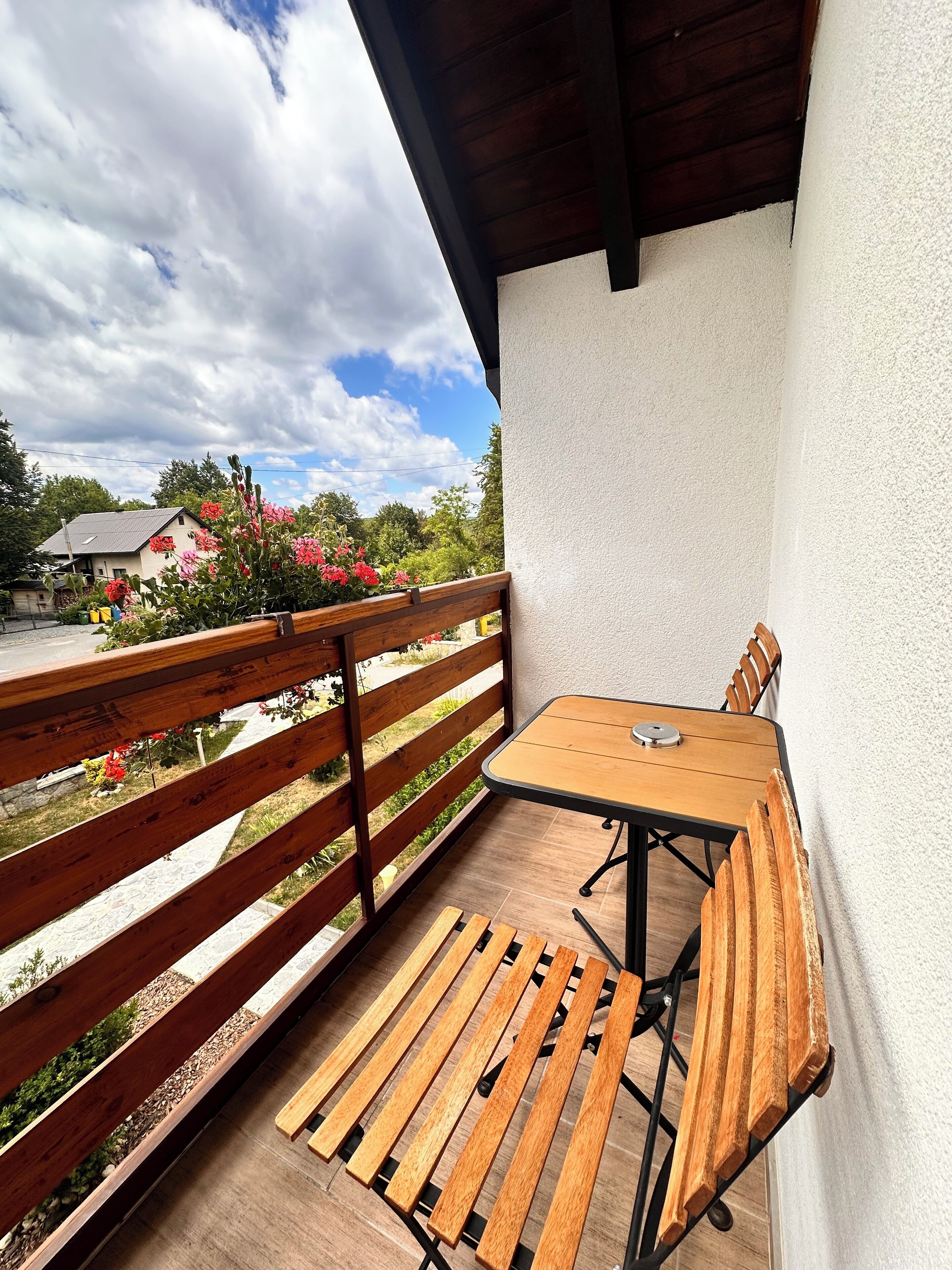 A wooden bench and table under a covered patio area with a view of a garden and a house.