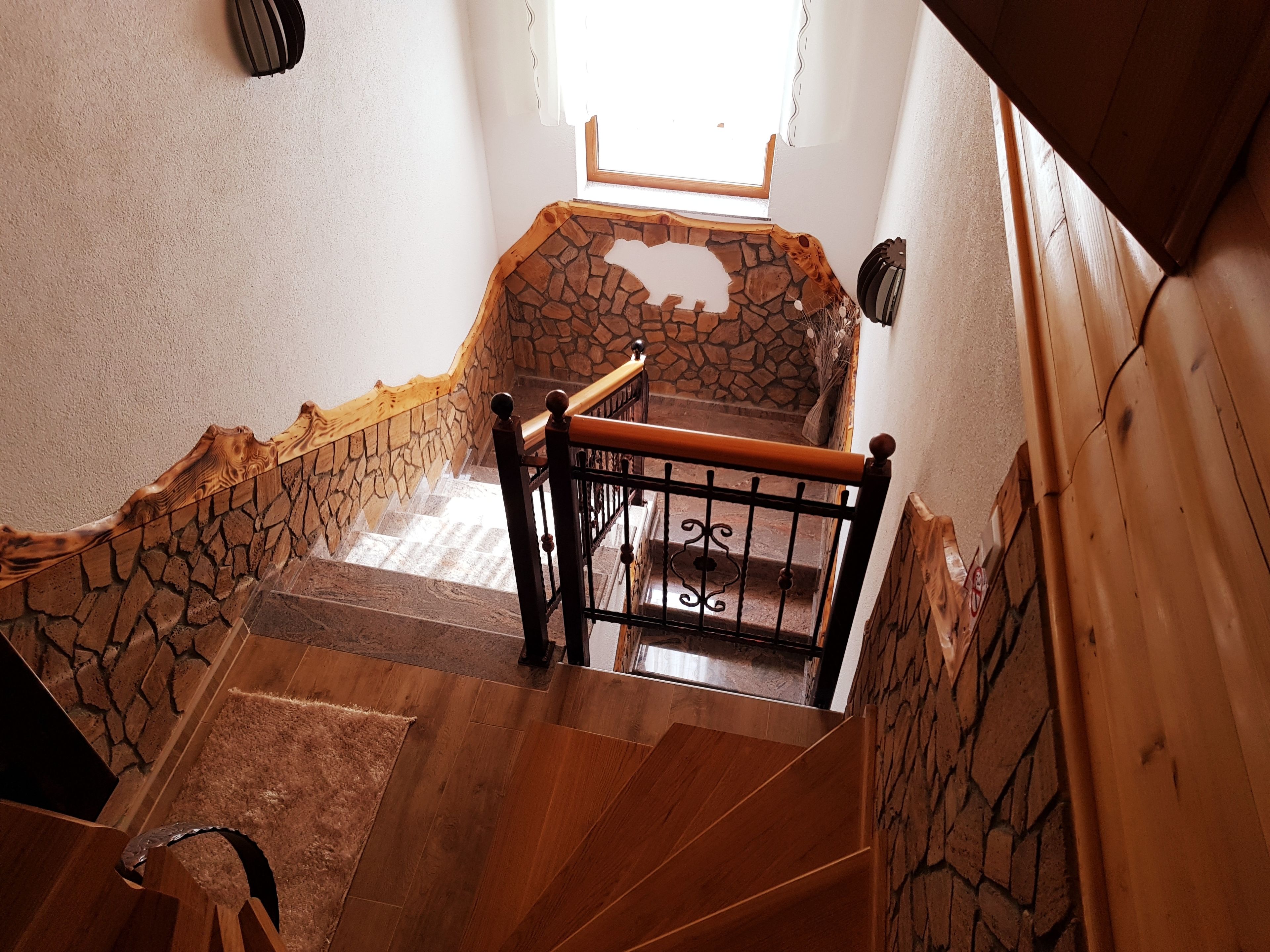 Un escalier en bois, avec un mur en pierre en haut, mène à une pièce dotée d’une fenêtre.