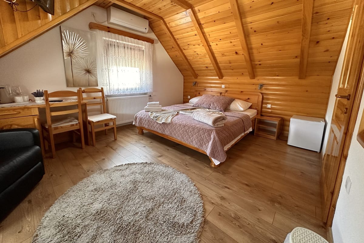 Un dormitorio acogedor en el ático, con techo de madera, cama con colcha acolchada, escritorio con silla y radiador.