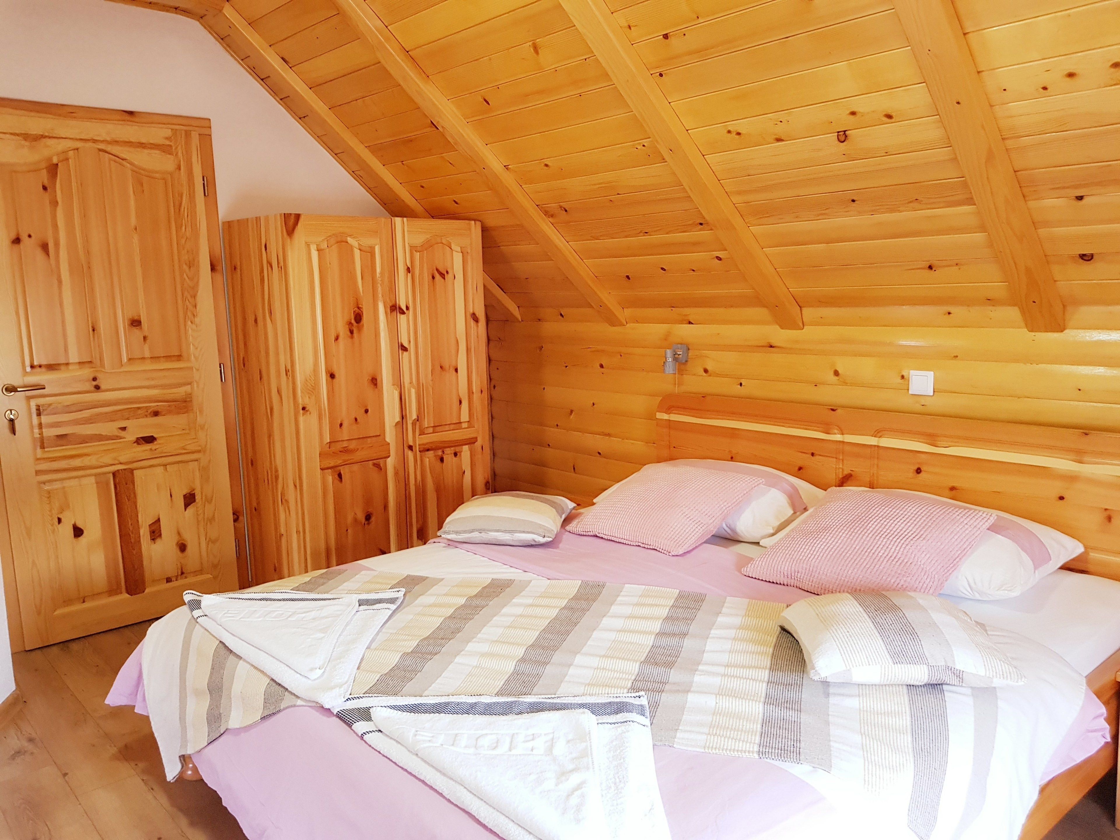 A wooden cabin bedroom with a bed, pillows, and a wardrobe.