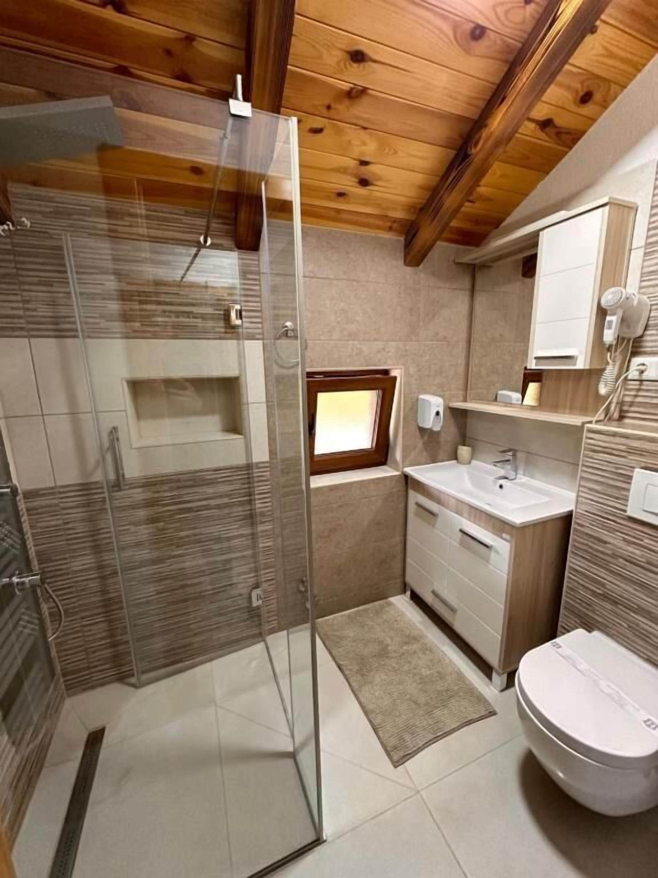 A modern bathroom with a glass shower enclosure, a sink, a toilet, and a small window.