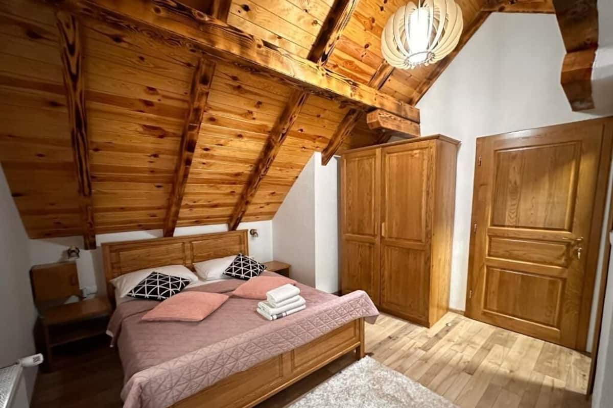 Un dormitorio con techo de madera, una cama con ropa de cama rosa, una mesita de noche y armarios de madera.