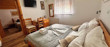A bedroom with a bed, wooden furniture, a television, and a window with curtains.