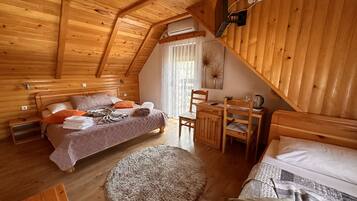 Un dormitorio acogedor en el ático, con techo inclinado de madera, una cama con almohadas y mantas, un pequeño escritorio de madera con una silla y una alfombra redonda en el suelo.