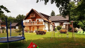 A playground with a slide, swings, and a trampoline in front of a wooden house with a balcony. - Plitvice Green Valley (Plitvicka Jezera)
